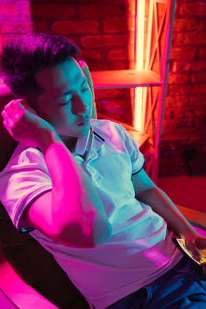 Young Korean man in headphones at home interior in gradient pink neon lightの写真素材