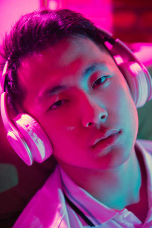 Close up young Korean man in headphones at home interior in gradient pink neon lightの写真素材