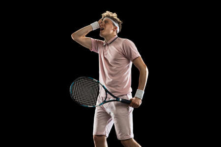 Young Caucasian man, professional tennis player isolated on black background.
