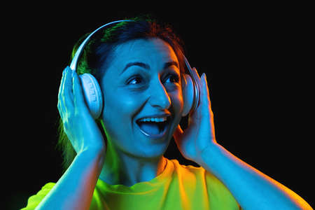 One beautiful woman in headphones isolated on dark background in neon lightの写真素材