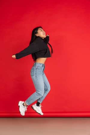 One happy Asian young girl jumping isolated on red studio background.