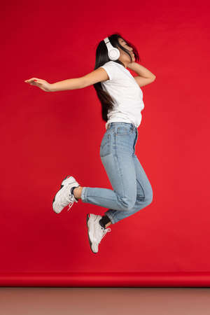 One happy Asian young girl jumping isolated on red studio background.の写真素材