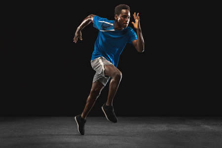Young African-American man, athlete training isolated over black background.