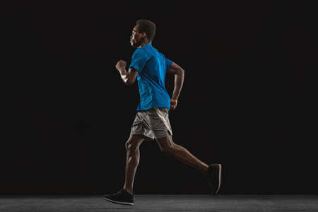Young African-American man, athlete training isolated over black background.