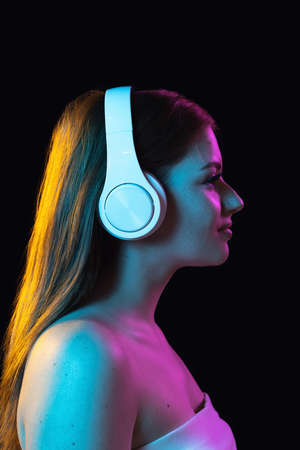 Portrait of young beautiful girl in headphones isolated over dark background.の写真素材