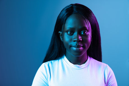 One young African beautiful girl isolated over dark background in mixed neon light.