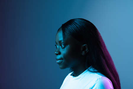 Smiling young African beautiful girl isolated over dark background in mixed neon light. Side viewの写真素材