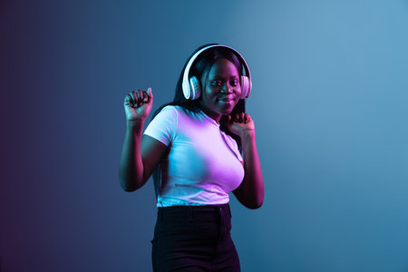 Portrait of young African beautiful girl isolated over dark background in mixed neon light.