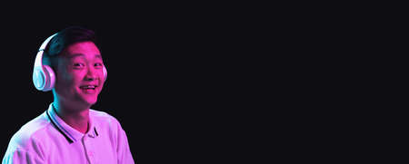 Asian young mans portrait isolated on dark studio background in neon light.の写真素材