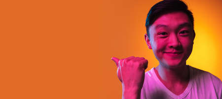 Close-up Asian young man isolated over gradient orange yellow background in neon light.の写真素材