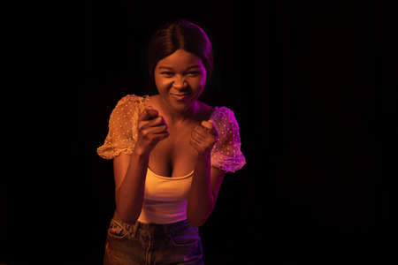 Portrait of young African beautiful girl isolated over dark background in mixed neon light.