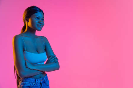 Portrait of young beautiful African girl isolated on pink background in neon light. Side view