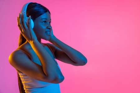 Portrait of young beautiful African girl isolated on pink background in neon light. Side viewの写真素材
