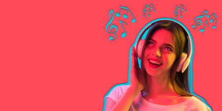 Close up beautiful girl in headphones isolated on pink background in neon lightの写真素材