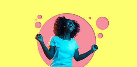 Young beautiful happy African-American girl isolated on yellow pink background in neon.の写真素材