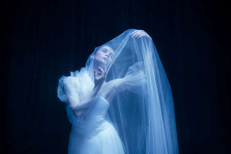 Loneliness. Young graceful beautiful woman, balerina in white wedding dress in art performance.