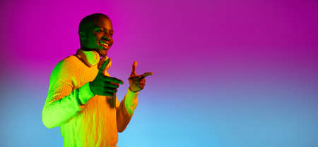 Flyer. Portrait of young African handsome man posing isolated over studio background in gradient neon lightの写真素材