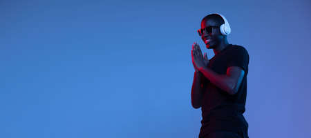 Portrait of young African handsome man posing isolated over dark background in mixed neon light. Flyerの写真素材