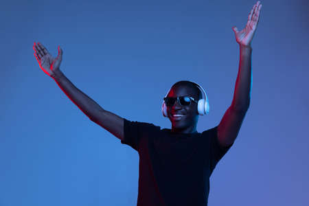 Portrait of young African handsome man posing isolated over dark background in mixed neon light.の写真素材