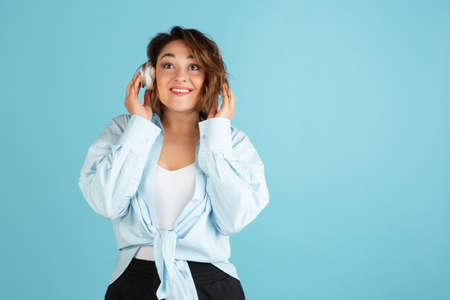 Happy young Caucasian beautiful woman in casual clothes and headphones isolated on light blue background.の写真素材