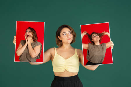 One young beautiful woman holding her portraits pictures isolated on green background.の写真素材