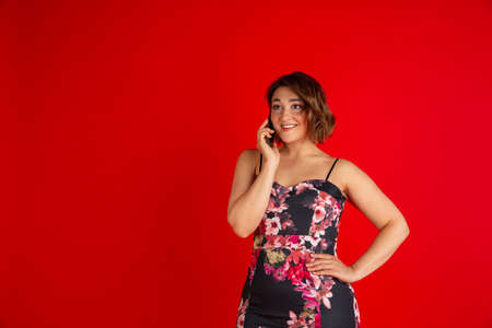Half length portrait of young Caucasian beautiful woman in bright dress isolated on bright red background.の写真素材