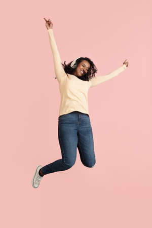 Full-length portrait of young beautiful girl in casual clothes jumping isolated on pink background.