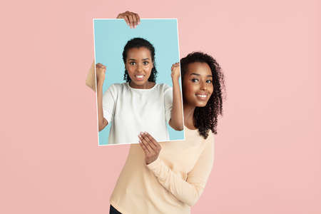 Young attractive girl holding her portrait, photo isolated on light pink background. Human emotion conceptの写真素材