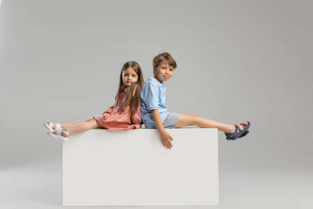 Two kids, brother and sister sitting on the box isolated solated over gray studio background.の写真素材