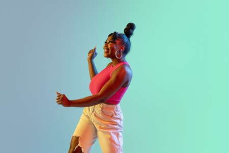 Young beautiful happy African girl isolated on blue-green background in neon.の写真素材