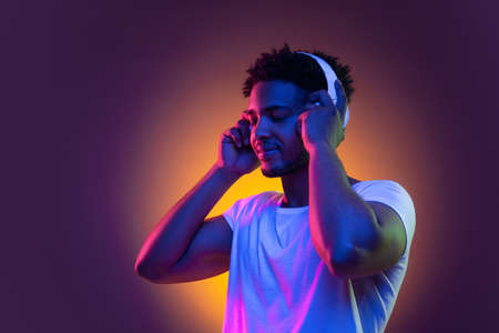 Portrait of a young african man at studio. Male model with headphones in bright neon lights. Art design concept.の写真素材