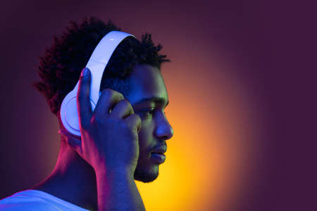 Portrait of a young african man at studio. Male model with headphones in bright neon lights. Art design concept.の写真素材