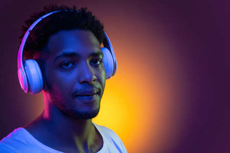 Portrait of a young african man at studio. Male model with headphones in bright neon lights. Art design concept.の写真素材
