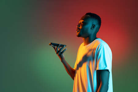 Young african man using smartphone in neon light on gradient background.