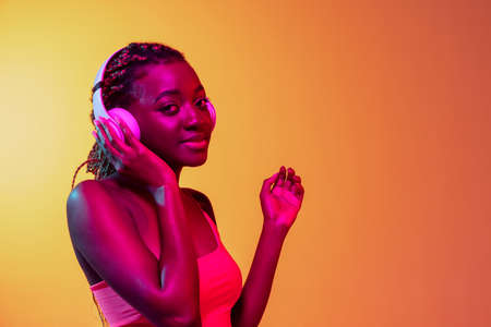 Joyful young beautiful African girl, female fashion model isolated on yellow background in neon light.の写真素材