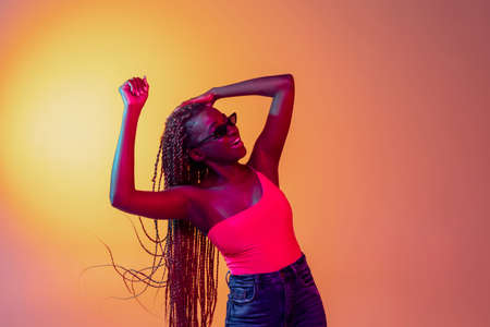 Joyful young beautiful African girl, female fashion model isolated on yellow background in neon light.の写真素材