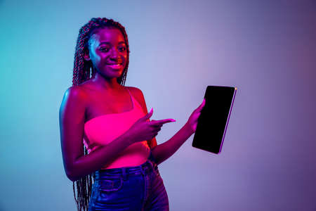 Young African woman with afro hairstyle isolated over lilac neon background. Studio shot. Concept of facial expression and human emotionsの写真素材