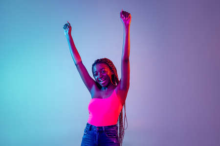 Young African woman with afro hairstyle isolated over lilac neon background. Studio shot. Concept of facial expression and human emotionsの写真素材