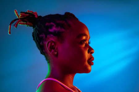 Smiling young African beautiful girl isolated over blue background in mixed neon light. Side viewの写真素材