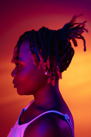 Smiling young African beautiful girl isolated over bright studio background in neon light. Side view