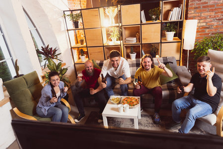 Bet for winner. Young men watching TV, sport match together. Concept of friendship, leisure activity, emotionsの写真素材