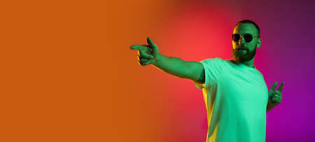 Flyer. One handsome bearded young man in sunglasses pointing isolated over gradient orange pink background in neon lights.の写真素材