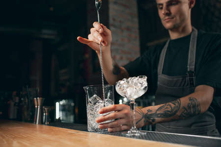 Young caucasian guy, professional bartender in apron mixing cocktails in pub or cafe.の写真素材