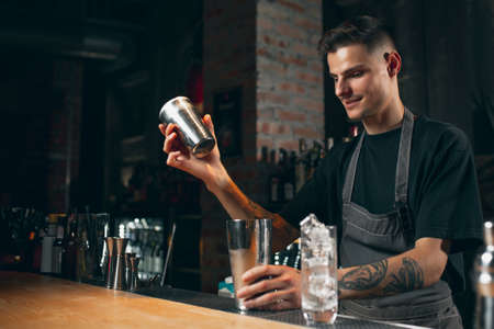 One young handsome bartender shaking an alcohol drink in cocktail shaker enjoying his job.の写真素材