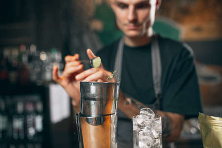 Young caucasian guy, professional bartender in apron mixing cocktails in pub or cafe.の写真素材