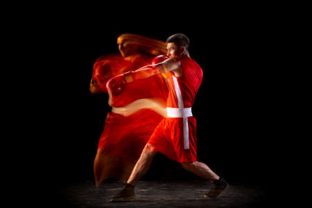 Full length portrait of one professional boxer in action, motion over black background in mixed lights. Side viewの写真素材