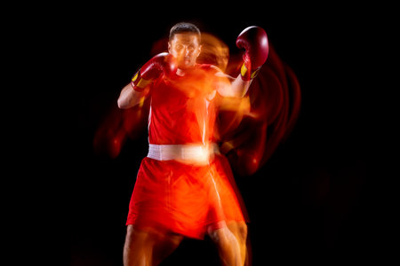 Front view of one professional male boxer in motion, action on black studio background in mixed...