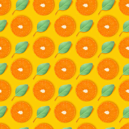 Modern art collage. Juicy slices of orange and small green leaves arranged in even rows over bright yellow background.の写真素材