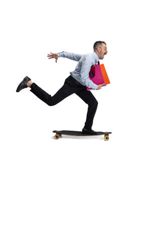 Late for meeting. Portrait of young Caucasian man, office worker rides on skateboard isolated on white background.の写真素材