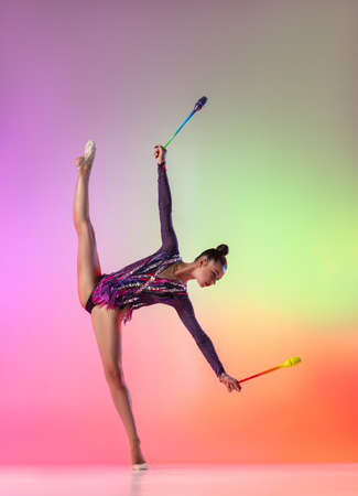 One female rhythmic gymnast with clubs in motion and action isolated on multicolored neon background.の写真素材